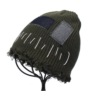 Close-up of military green knitted beanie featuring denim patches and distressed brim details