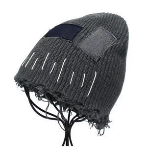Detail view of distressed dark grey knit beanie featuring vintage denim patches and fringe