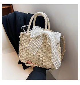 Détail du sac en paille tissé avec nœud en dentelle blanche et poignées rondes robustes