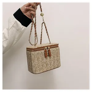 Vue détaillée du sac boîte en paille tissée avec bandoulière chaîne et boucle dorée