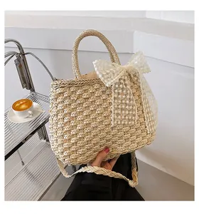 Gros plan du sac cabas en paille avec un grand nœud en dentelle et bandoulière tissée