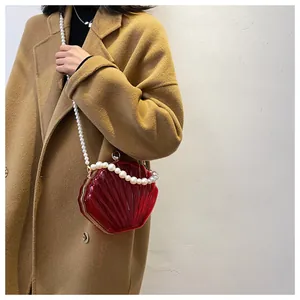 Elegante borsa a conchiglia rossa in acrilico con tracolla di perle su cappotto beige