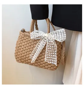 Détail du sac cabas en paille tissée avec nœud en dentelle blanche et anses tressées
