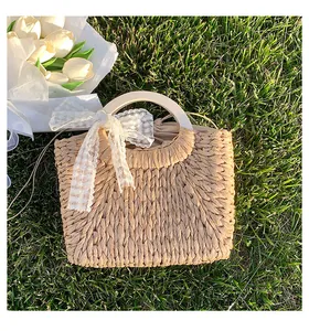 Detail of straw woven beach bag with white lace bow and tulips on green lawn