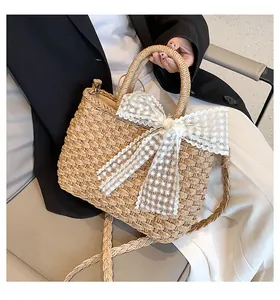 Détail d'un sac cabas en paille fait main avec nœud en dentelle blanche et bandoulière