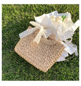 Detailed view of woven straw bag with floral lace bow and white handles on grass