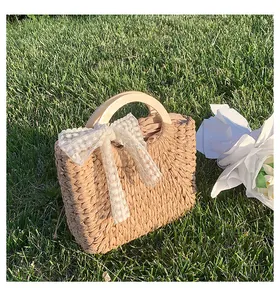 Detail of straw woven tote bag with wooden handle and lace bow on a grass lawn