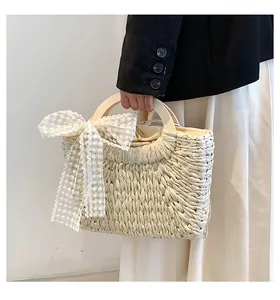 Detail of hand-woven straw tote bag with large white lace bow and wooden handle