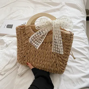 Large woven straw tote bag with round wooden handles and a white lace bow decoration