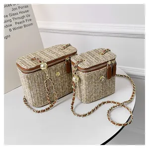 Détail du sac boîte en paille tressée avec bordure en cuir marron et fleur dorée