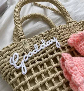 Detail of hand-woven straw tote with white Goodday embroidery and pink crochet flower