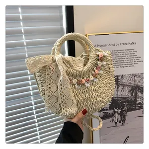 Dettaglio borsa da spiaggia in paglia beige con decori floreali e fiocco in pizzo