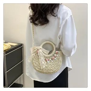Dettaglio borsa in paglia intrecciata con piccoli fiori e un fiocco in pizzo decorativo