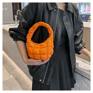 Detail view of bright orange quilted puffy handbag showing soft nylon texture and handle