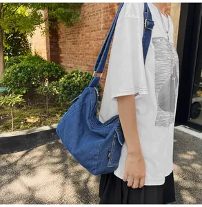 Blue denim crossbody tote bag featuring a wide adjustable strap and side pocket detail