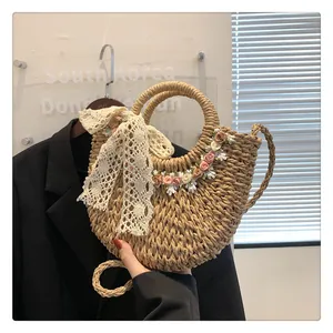 Dettaglio borsa in paglia intrecciata a mano con fiocco di pizzo bianco e decorazioni floreali