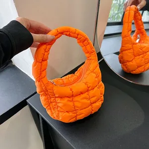 Quilted orange cloud bag with puffer texture and silver zipper shown on a modern table
