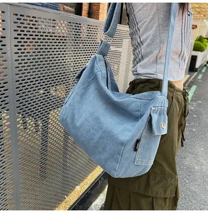 Blue denim tote bag with wide shoulder strap shown on model against a street background