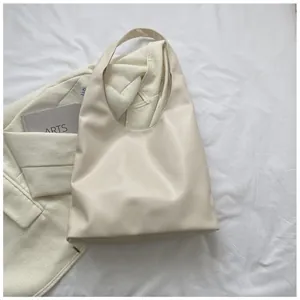 Detail shot of a cream-colored minimalist hobo tote bag on soft white fabric