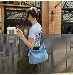 Detail of light blue denim crossbody bag featuring functional side flap pocket and texture