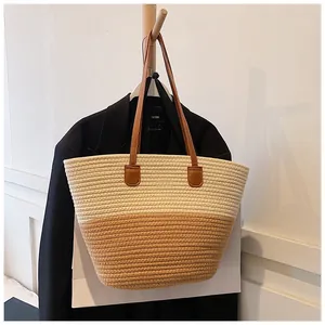 Detail of a large two-tone straw tote bag with brown leather handles on a hanger