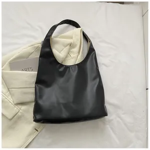 Top view of a black minimalist hobo bag with matte finish on white bedding backdrop