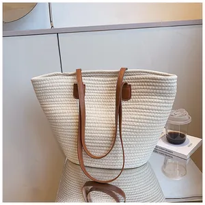 Close-up of beige woven tote bag with brown leather straps on a reflective surface