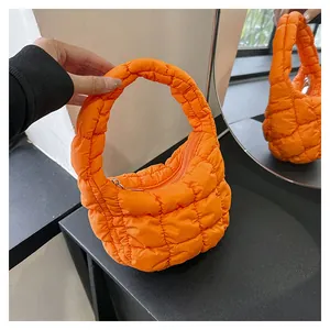 Detail of a bright orange quilted puff handbag with soft nylon texture and metal zipper