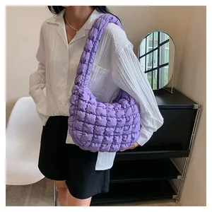Close-up of purple quilted puffy shoulder bag with square texture on model