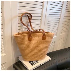 Detailed close-up of a woven straw tote bag with brown leather handles on a white book