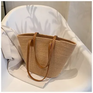 Detail of a large straw tote bag with brown leather handles on a white chair