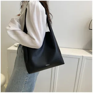 Detailed view of black matte leather tote bag with white logo worn by a model