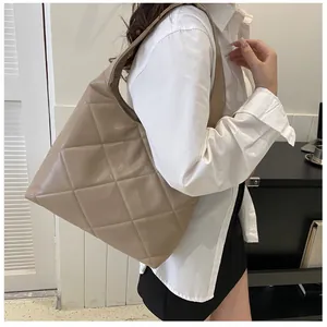 Detail of beige quilted tote bag with large diamond pattern and glossy finish on model
