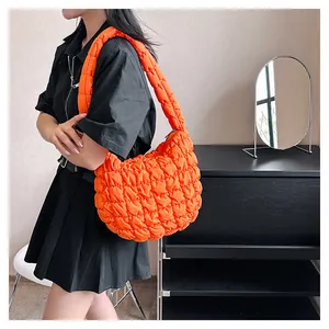 Model wearing a bright orange puffer shoulder bag with quilted fabric and texture
