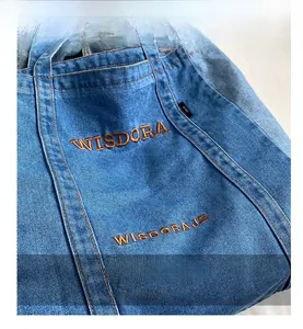 Detailed macro view of WISDORA denim tote bag featuring orange brand embroidery and stitching