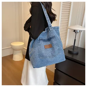 Detail of blue denim tote bag featuring a leather patch and spacious outer pocket