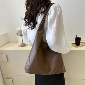Large dark brown leather tote bag with soft texture worn as a stylish shoulder bag