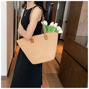 Close-up of woven straw tote bag with brown leather shoulder straps and large capacity