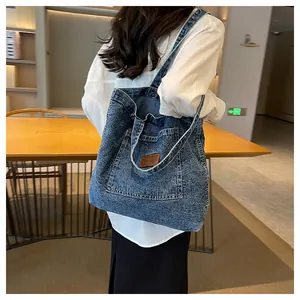 Detailed close-up of blue denim tote bag with brown faux leather patch and large front pocket