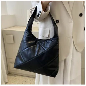 Detail view of large black quilted tote bag with diamond pattern on model's shoulder