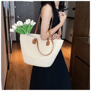 Detail of spacious straw tote bag with brown leather straps and woven cream texture