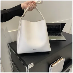 Close-up of minimalist off-white leather tote bag with AIBEIDA logo in office setting