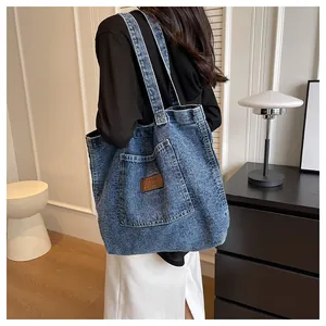 Detail shot of a large denim tote bag worn by a model in a cozy indoor setting