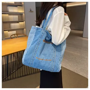 Close-up of a blue denim tote bag with orange embroidery worn by a model in a study