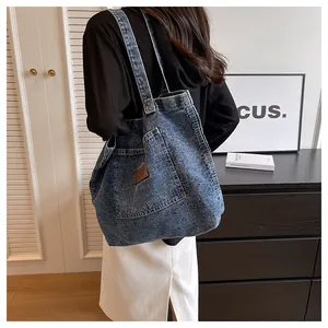 Detailed view of washed blue denim tote bag with brown leather patch and wide shoulder strap