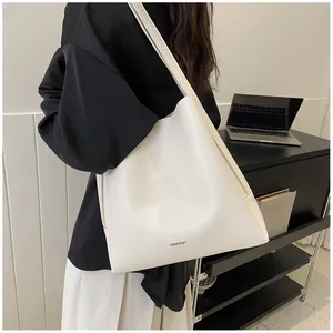 Minimalist white leather tote bag shown on shoulder in a professional office setting