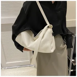 Gros plan d'un sac à bandoulière en cuir crème texturé porté avec une tenue de bureau