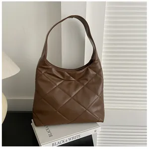 Close-up of brown quilted hobo bag with detailed stitching on minimalist white books