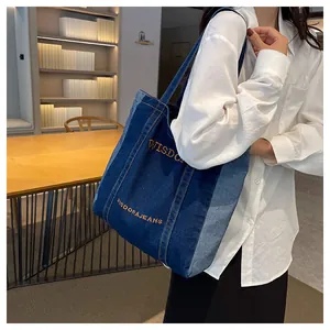 Detail of denim tote bag showing bicolor denim panels and orange WISDORA letter embroidery