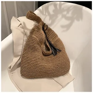 Detail of a brown woven straw tote bag with side tassels on a modern white chair